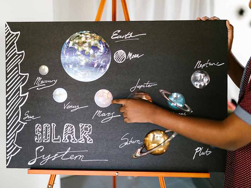 Presentation board of the solar system with a young student pointint to a planet