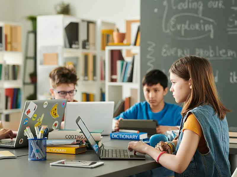 Young female student using a laptop with other students in the background.