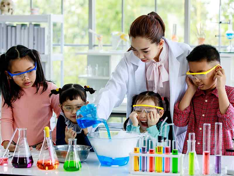 Teacher in a lab coat helping students do a chemistry experiment