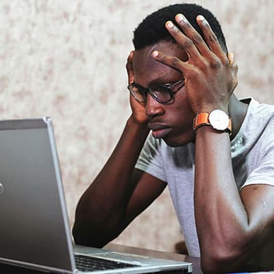 High school student holding head in hands, frustrated at computer