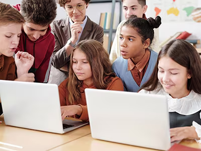 Elementary students using a computer with classmates watching. 