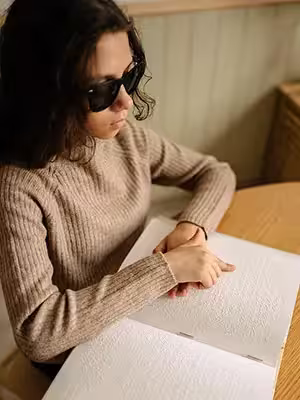 A young child wearing sunglasses and reading a braille book