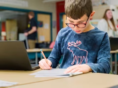Young man writing next to a computer.
