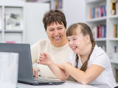 Caregiver and student smiling while working on laptop.