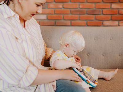 Parent with toddler with light skin and white hair exploring a child's tablet.